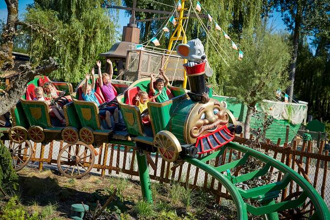 Eine Gruppe von Menschen fährt in einer bunt gestalteten und fröhlichen Achterbahn in einem Freizeitpark.