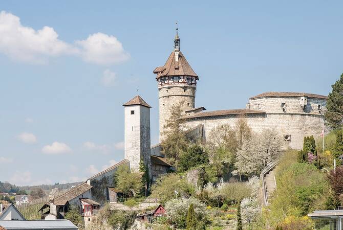 2 alte Türme einer Burg mit Burgmauer auf einem Hügel, mit blauem Himmel im Hintergrund