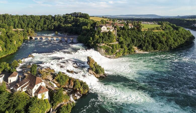 Blick auf den Rheinfall aus der Luft, an beiden ufern stehen alte Häuser um geben von grünen Bäumen