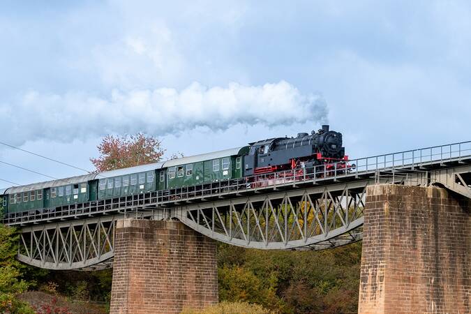 ein historischer Zug mit Dampflok fährt über eine Eisenbahnbrücke