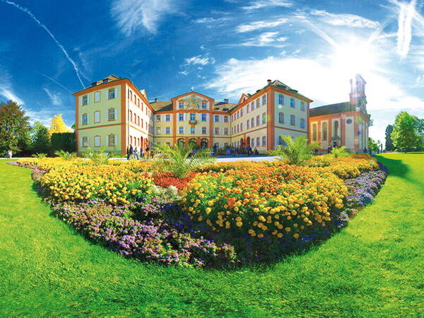 das Schloß mit Kirche auf der Insel Mainau unter blauem Himmel mit leichten Schleierwolken, im Vordergrund ein buntes Blumenbeet