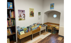 Eine Leseecke für Kinder mit einem Holzboden. Zu sehen sind Bücherregale und Kisten. 