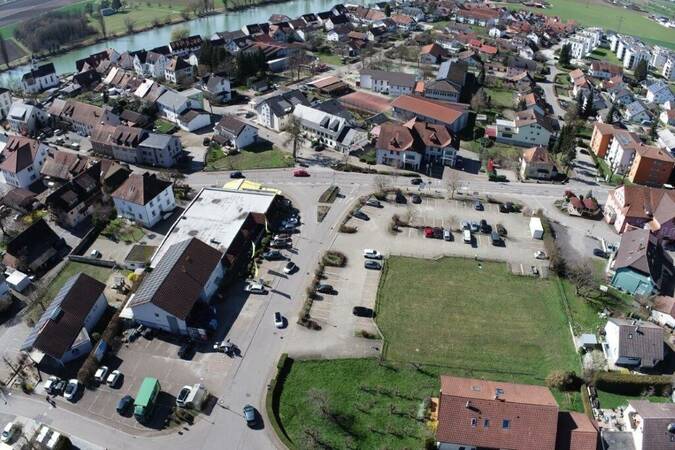 Luftbild des Ortskerns Kadelburg, Kreuzungsbereich, Straßenverlauf der Ortsdurchfahrtsstraße Hauptstraße mit Kreuzung in die Kirchstraße und Deckwiesenstraße. Ansicht von oben auf umliegende Wohnhäuser, das Apotheken- und Sparkassengebäude, zentral mittig das große EDEKA Einkaufsgebäude und Park- und Grünflächen sowie links im Bild ein Arztpraxisgebäude. Im Hintergrund sieht man den Rheinverlauf.