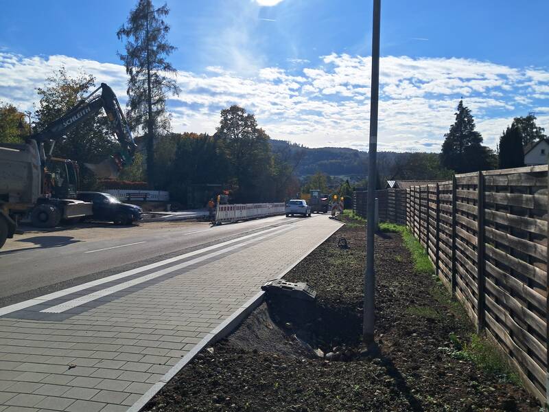 Blick auf den Straßenverlauf der Ortseinfahrt von Danstetten her kommend nach Rheinheim Kreisverkehr auf Höhe Friedhof, im Vordergrund die neu sanierte Bushaltestelle, rechts im Bild ein Bagger. 