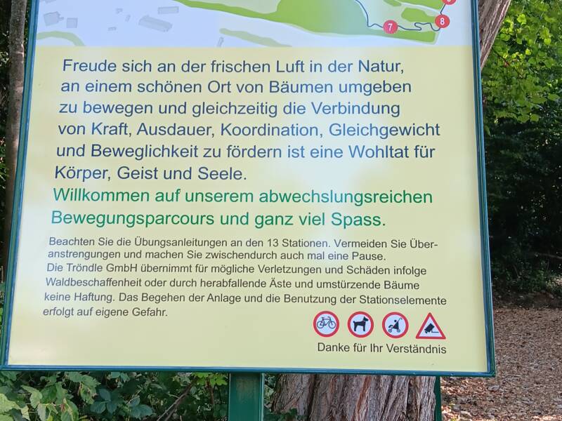 Ein Schild im Wald informiert über einen 2,2 km langen Bewegungsparcours mit 13 Stationen und Tipps für eine sichere Benutzung.