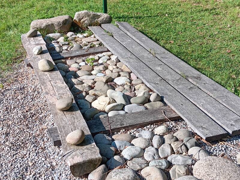 Ein Pfad aus Holzbohlen und großen Steinen befindet sich im Freien, begleitet von einem Schild mit Liegestütz-Anweisungen.