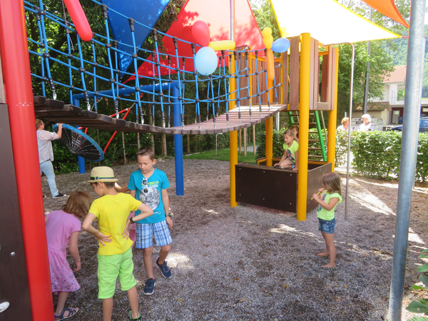 Sechs Kinder spielen im und unter einer Hängebrücke mit Spielturm