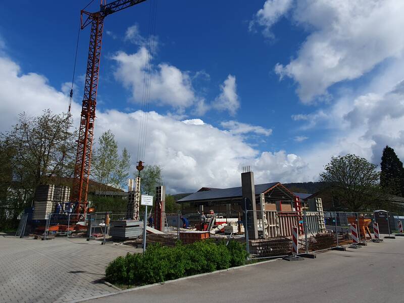 Bauplatz zwischen zwei Gebäuden und an einer Straße entlang verlaufend, ein großer Baukran steht auf der mit Absperrungen umsäumter Baustelle, verschiedene beginnende Bauarbeiten,