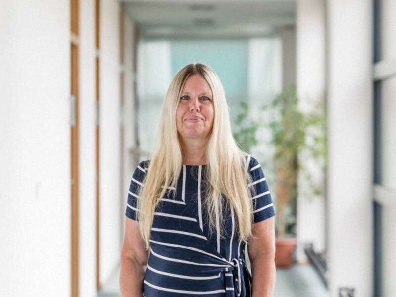 Frau mit blonden langen Haaren und blau/weiß geringeltem Shirt steht in einem langen Hellen Flur