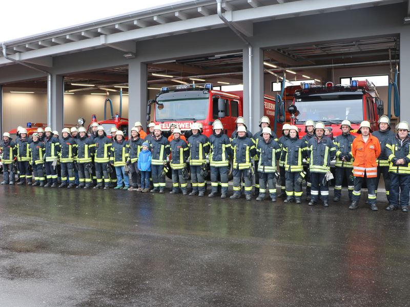 Gruppenfoto mit Mitgliedern der Freiwilligen Feuerwehr Küssaberg vor dem Feuerwehrhaus in Rheinheim mit geöffnetet Toren und dem Blick auf die darin stehenden Fahrzeuge im Hintergrund. 